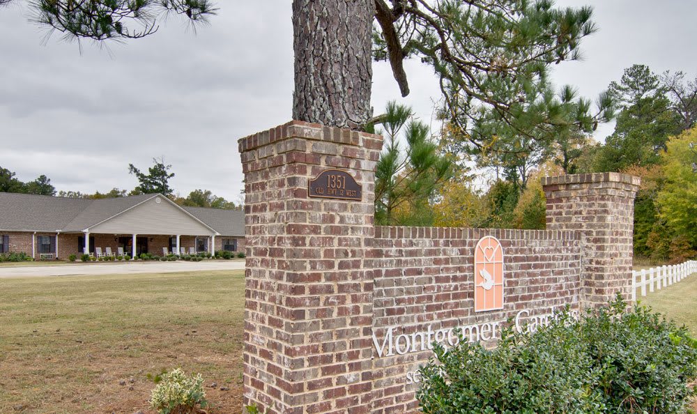 A brick pillar with a tree growing on top, displaying a sign near a residential building.