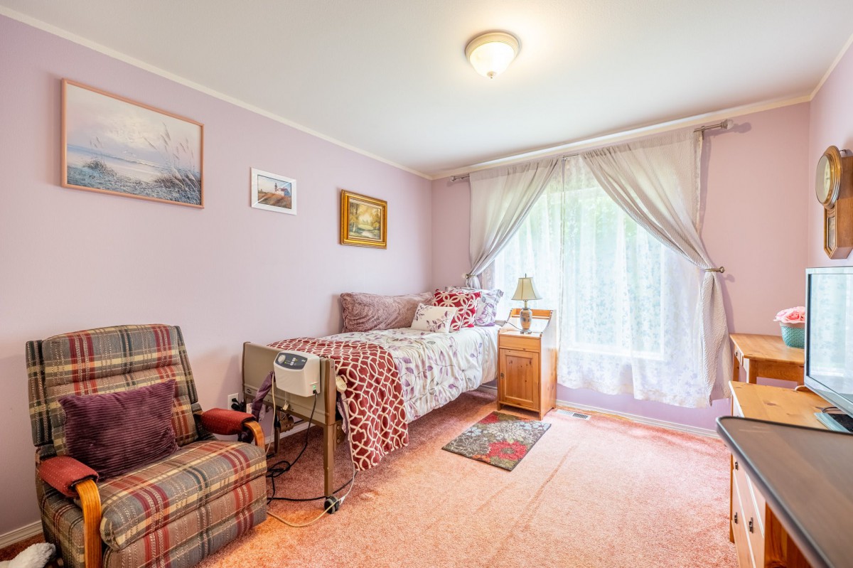 A cozy bedroom with pink walls, featuring a single bed and an armchair by the window.