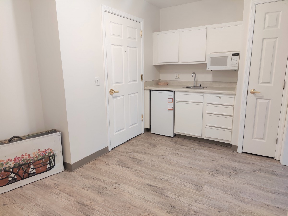 A minimalist kitchen featuring white cabinets and wooden flooring.