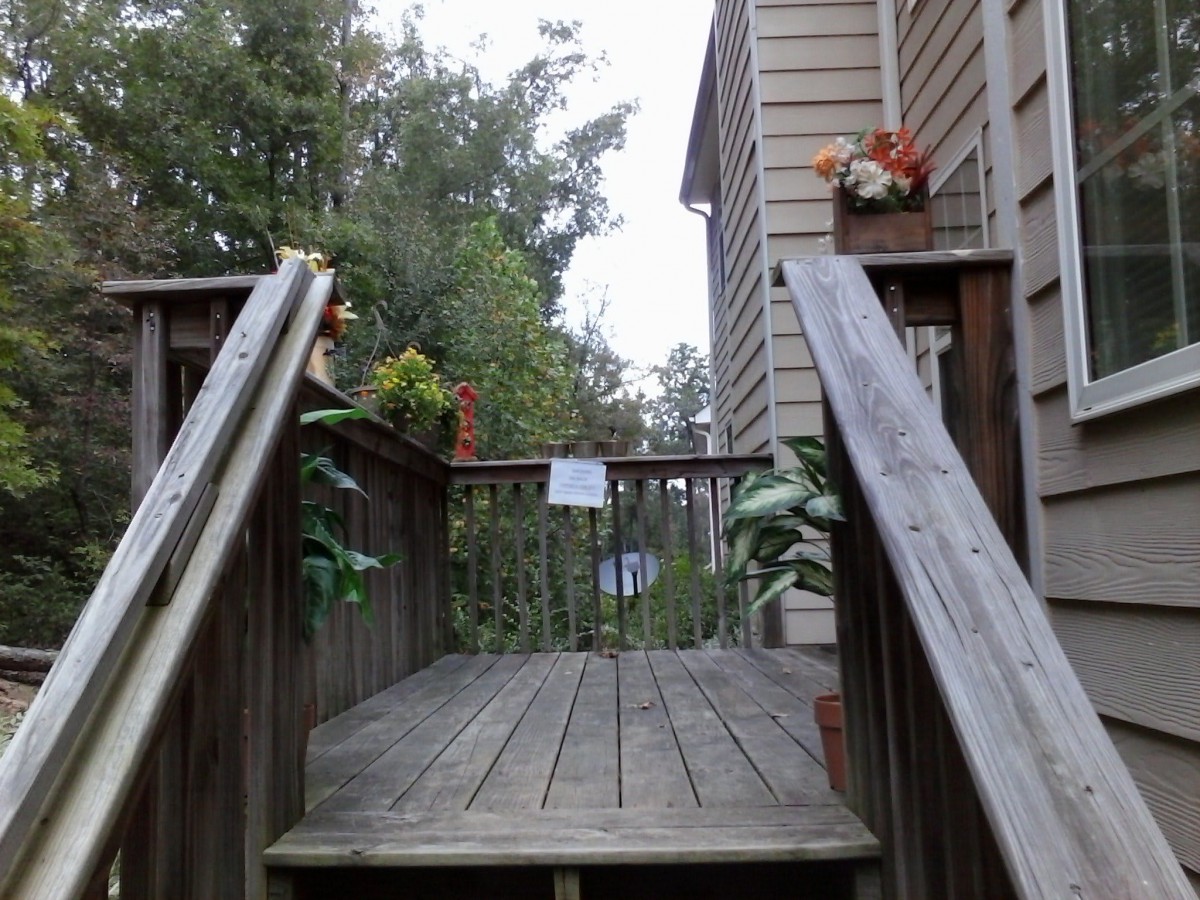 A wooden deck with stairs leading to a house, adorned with plants and flowers.