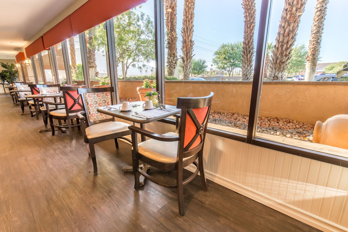 A cozy restaurant dining area with tables and chairs next to large windows, offering a bright and inviting atmosphere.