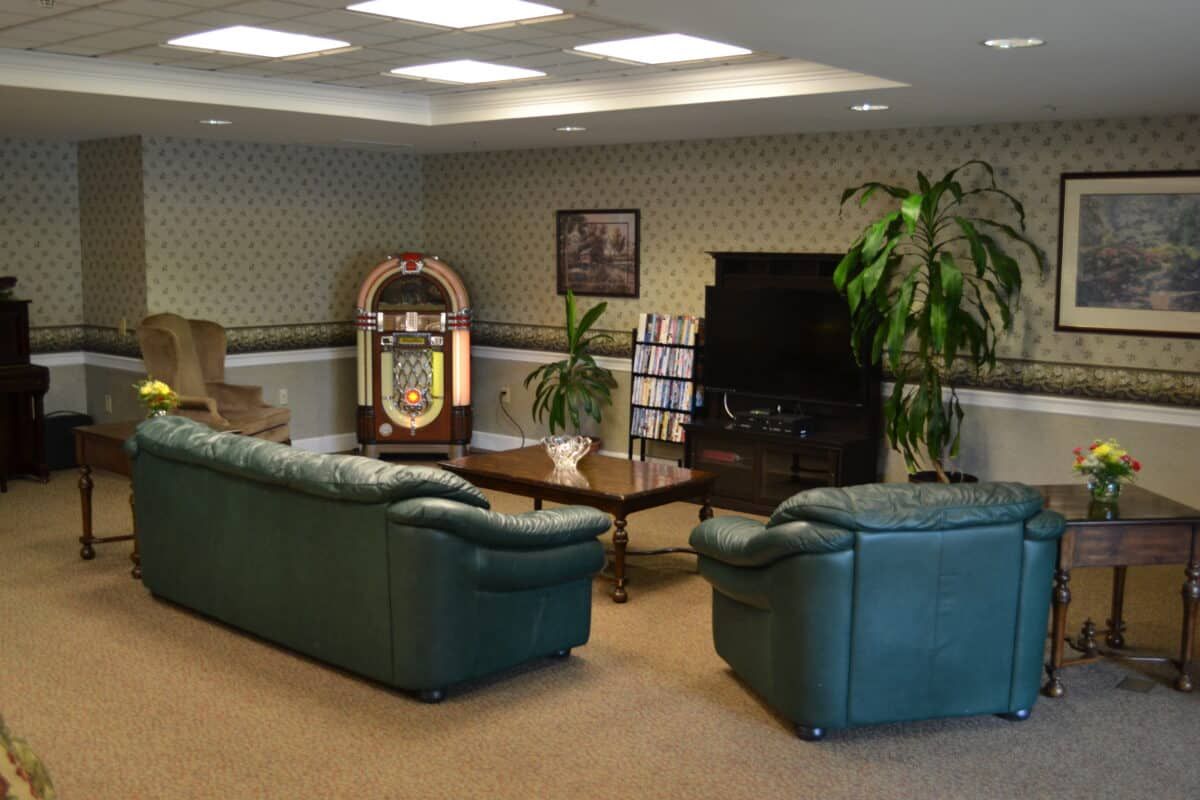 A cozy lounge area featuring green leather sofas, a classic jukebox, and potted plants.