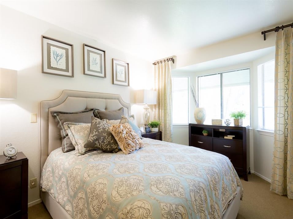 A well-decorated bedroom featuring a cozy bed with patterned bedding, a dresser near a window, and elegant drapes.