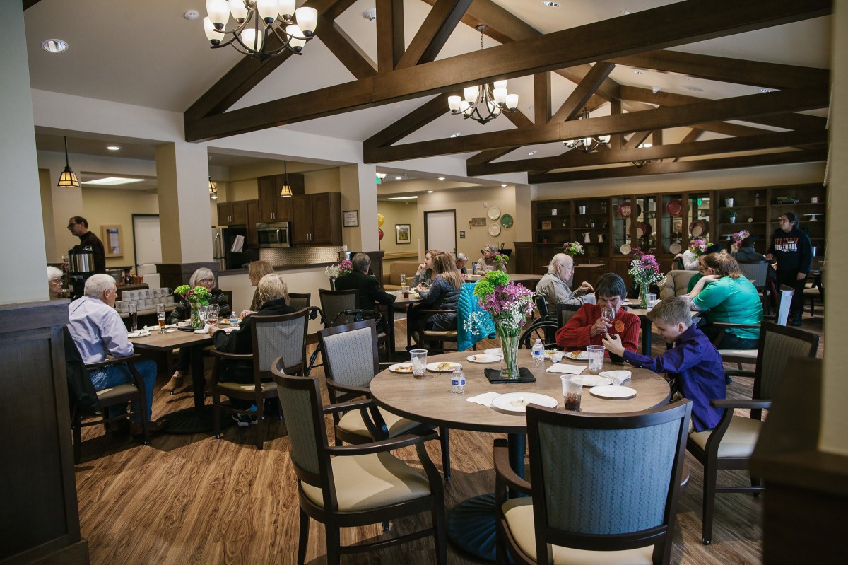 A communal dining area with wooden beams and chandeliers, where people are seated at tables.