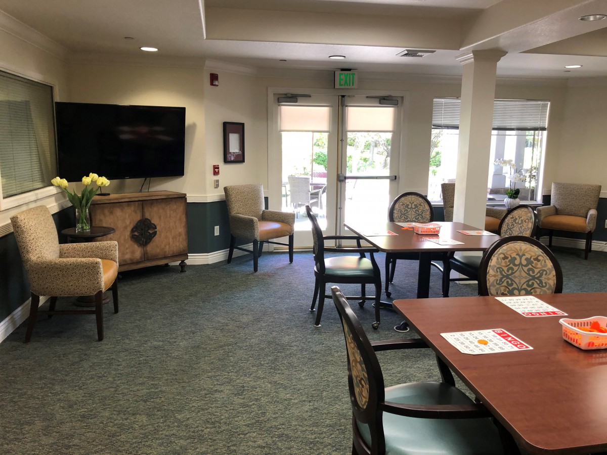 A bright common area with tables, chairs, and a TV.