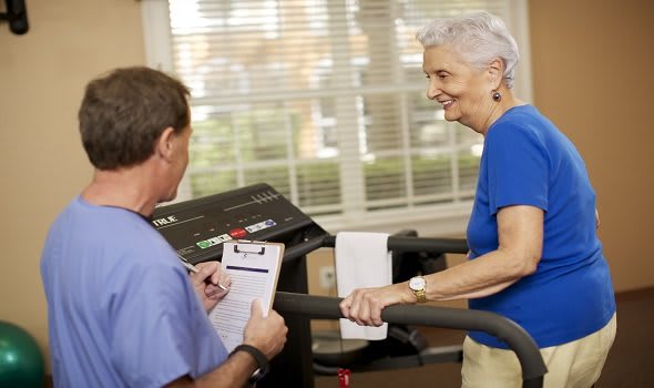 A senior woman engaging in physical therapy on a treadmill with assistance from a healthcare professional.