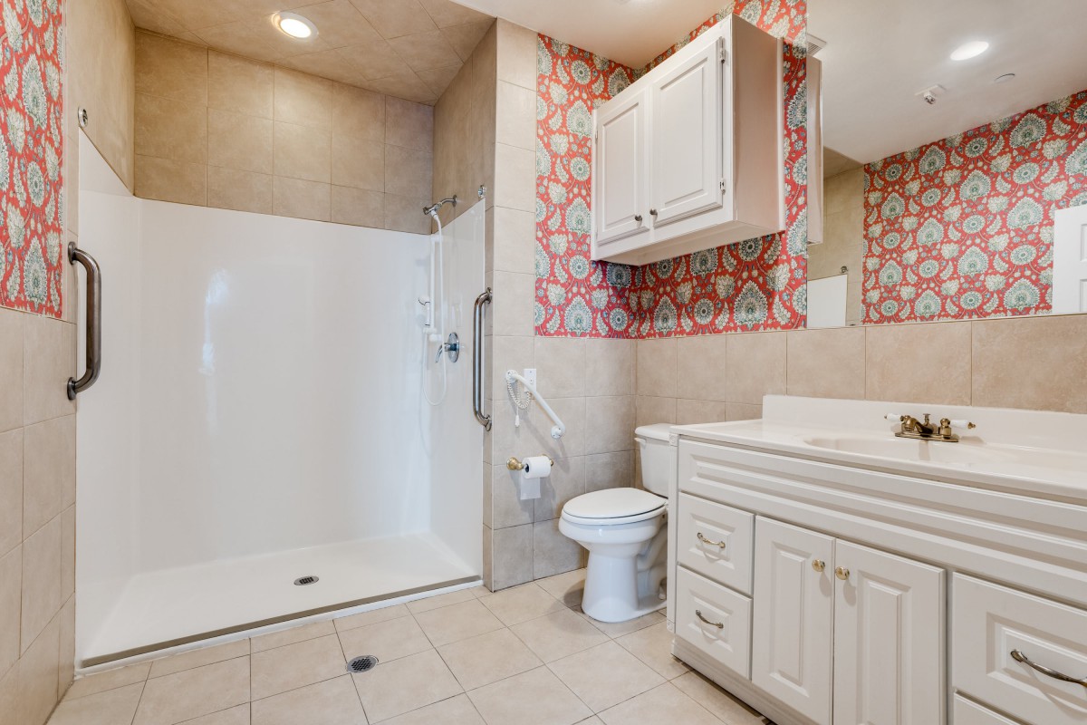 A modern bathroom featuring a walk-in shower, toilet, and sink with a cabinet set against decorative wallpaper.