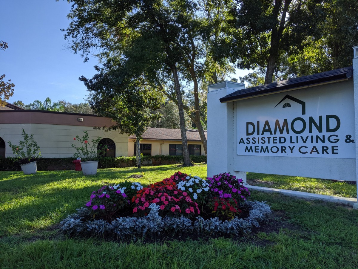 Entrance of a facility labeled 'Diamond Assisted Living & Memory Care' with landscaped flowers and trees.