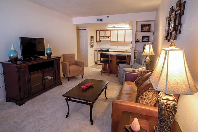 A cozy living room with a sofa, armchairs, and a view of the kitchen area.