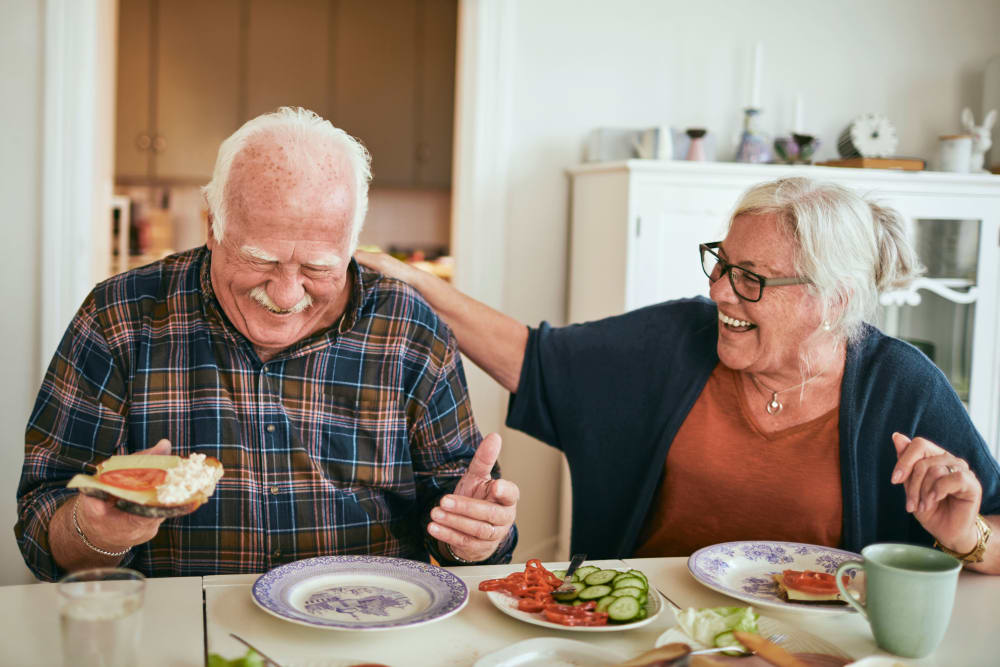 An elderly couple sharing a joyful moment while having a meal together at home.
