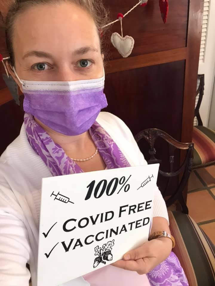 Person wearing a mask holding a sign that says '100% COVID Free Vaccinated'.