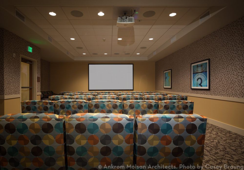 A small theater with patterned seating and a projection screen.