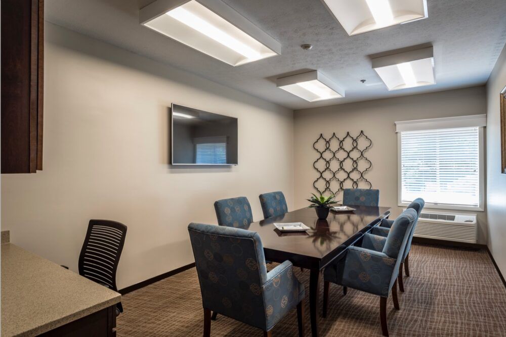 A modern conference room with a large table, chairs, and a TV screen on the wall.