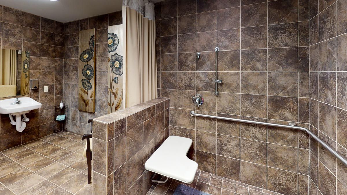 An accessible bathroom with a tiled shower area, featuring a wall-mounted shower seat and grab bar for safety.