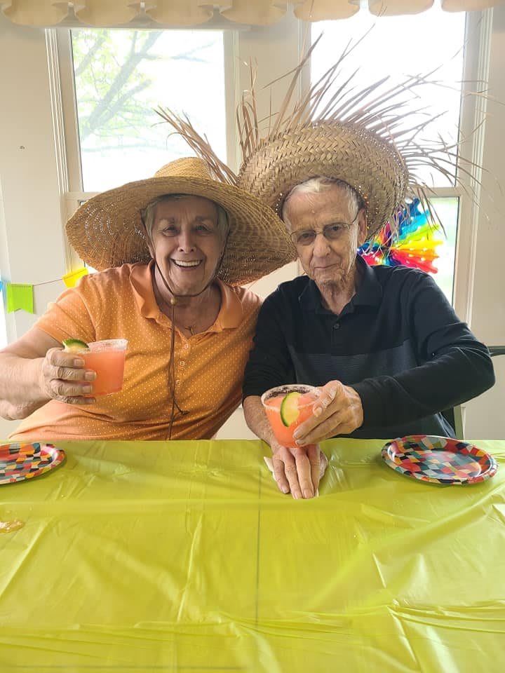 Two people wearing straw hats enjoy festive drinks at a tropical-themed party.