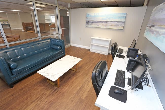 A modern office space with desks, computers, and a blue couch set against a wooden floor.