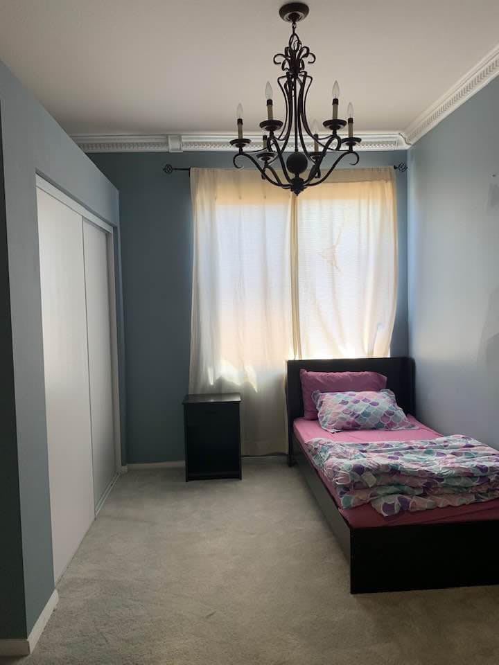 A minimalist bedroom with a single bed, chandelier, and soft curtains.