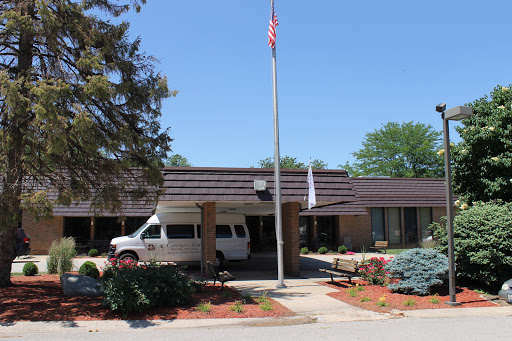 A view of a single-story building with an American flag, surrounded by well-maintained landscaping and a transportation van parked nearby.