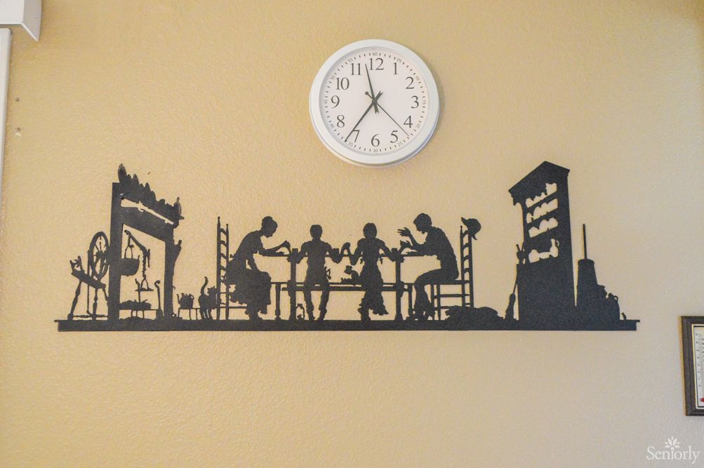 A wall featuring a round clock above a black silhouette sticker of people dining, set against an urban backdrop.