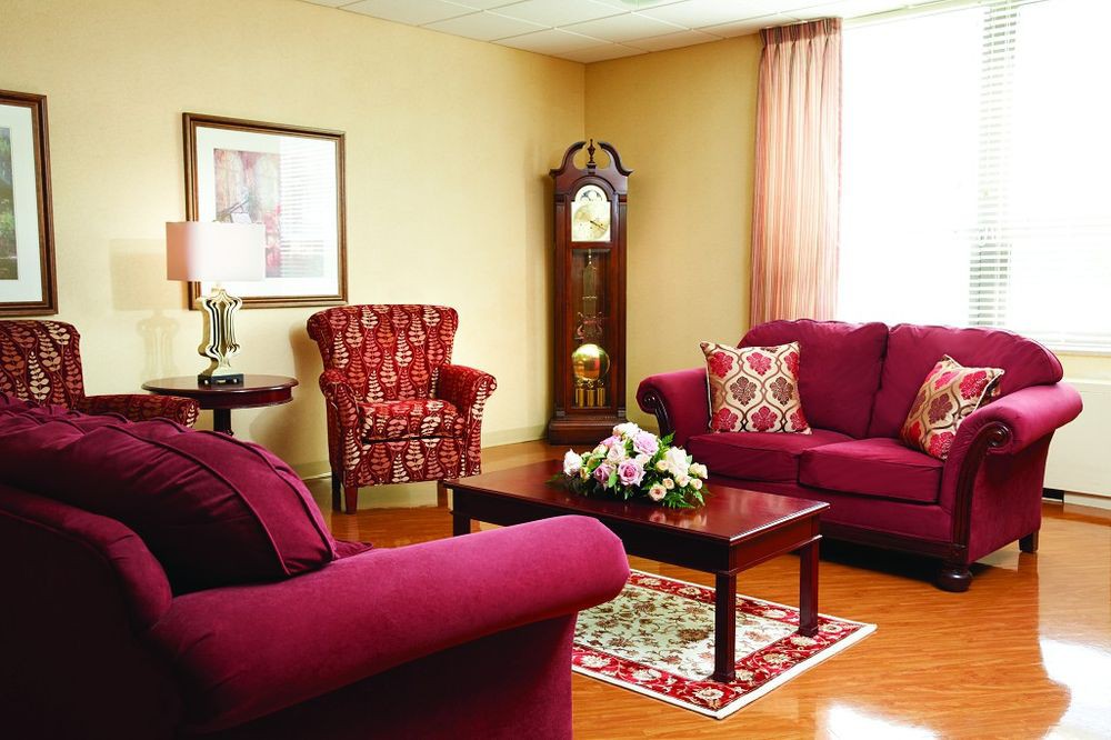 This is a cozy living room with plush red sofas, an armchair, a wooden coffee table, and a classic grandfather clock.