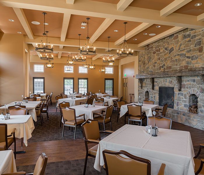 A spacious dining room with neatly arranged tables, elegant chandeliers, and a stone fireplace.