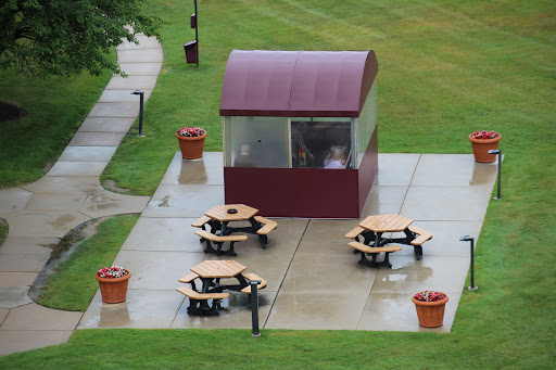 A cozy outdoor picnic area featuring a covered pavilion and several wooden tables set on a grassy lawn.