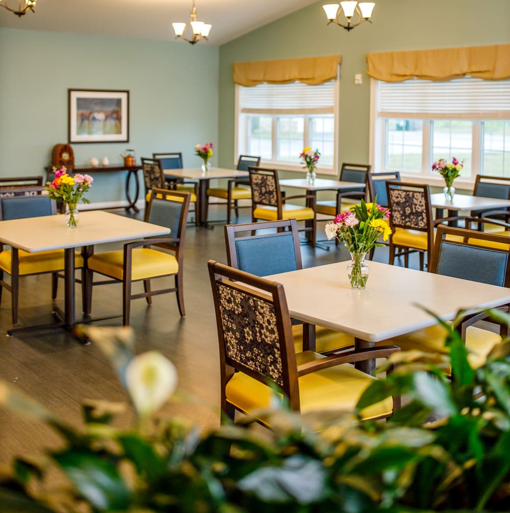 A well-lit dining room with neatly arranged tables and chairs, decorated with flowers.