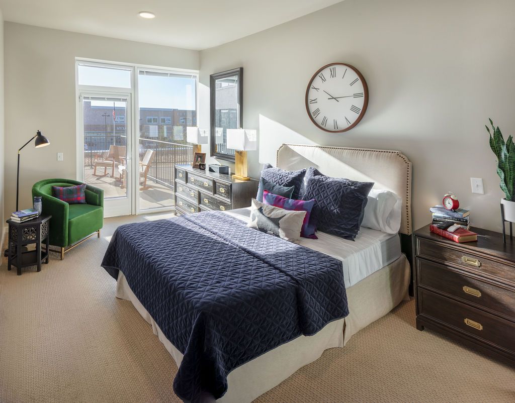 A modern bedroom with a bed, large wall clock, and a view of the balcony.