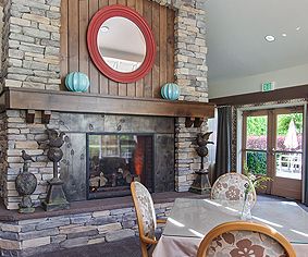 A cozy living room featuring a stone fireplace, adorned with a round mirror and decorative vases, complemented by a nearby table and chairs.