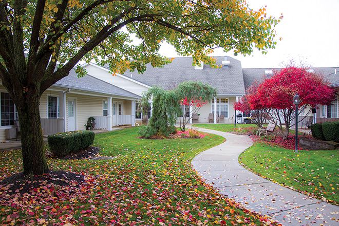 A serene garden pathway lined with colorful autumn leaves and surrounded by buildings.