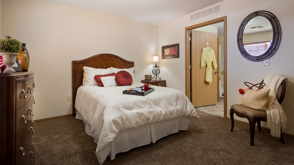 A cozy bedroom with a neatly made bed, featuring decorative pillows and a nightstand with a lamp.