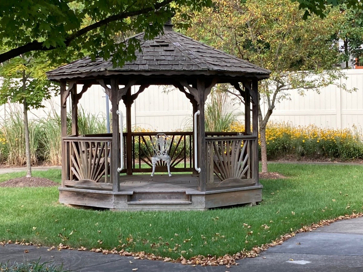 A wooden gazebo in a tranquil park setting, surrounded by trees and greenery.