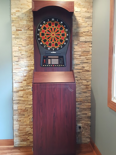 An electronic dart machine set against a stylish stone wall.