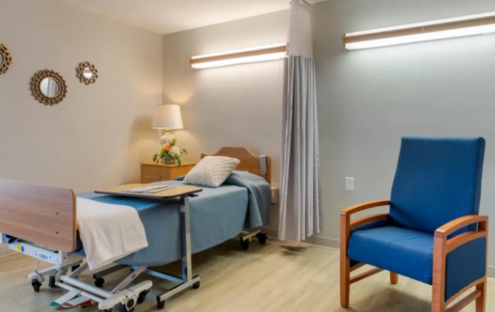 A clean and well-lit hospital room with a bed and chair.