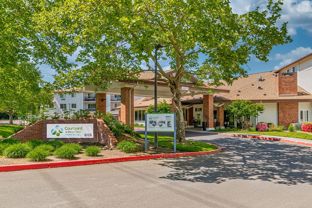 A well-landscaped building entrance surrounded by trees and a driveway.