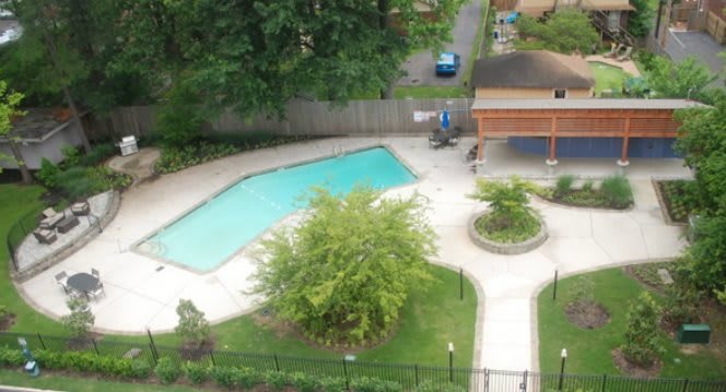 An aerial view of an outdoor swimming pool surrounded by greenery and walkways.