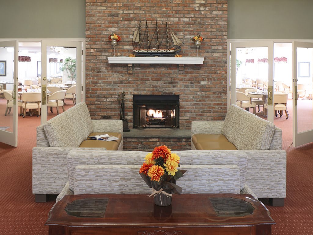A cozy living room with a brick fireplace, surrounded by comfortable couches and a coffee table adorned with colorful flowers.