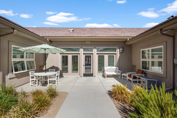 A sunny patio area with outdoor seating and landscaped surroundings in a residential building.