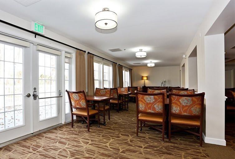 A spacious dining area with multiple tables and chairs, featuring modern lighting and large windows.