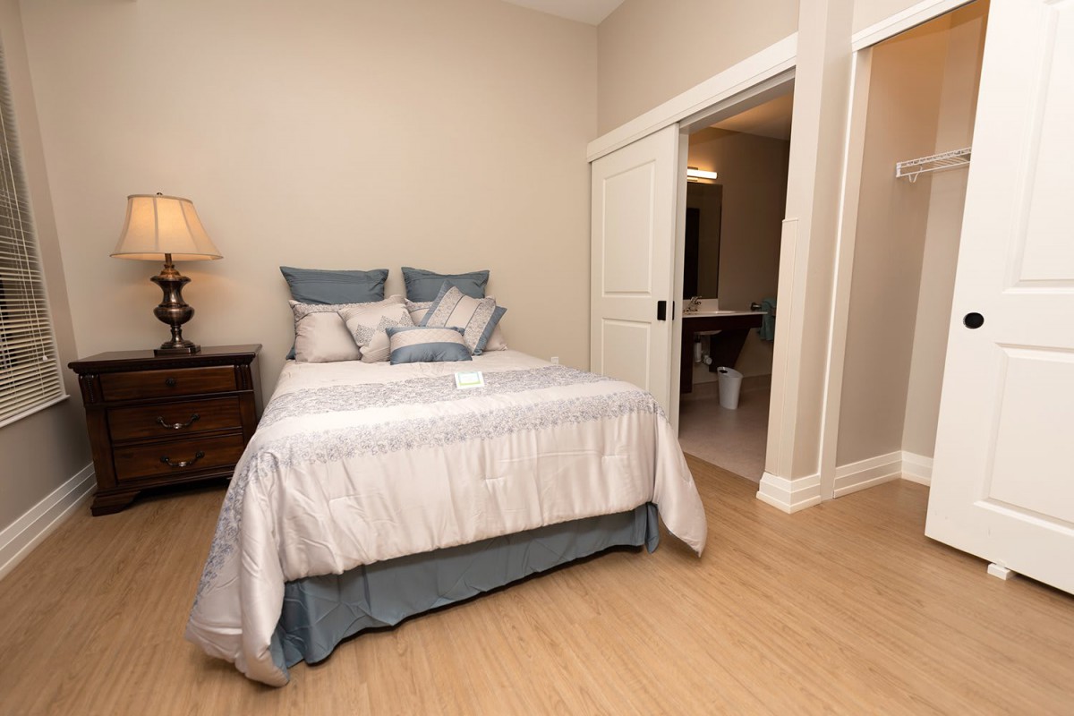 A neatly arranged bedroom with a bed, pillows, and a bedside lamp.