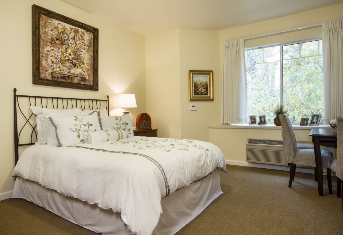A cozy bedroom with a large bed, a bedside lamp, and a window letting in natural light.