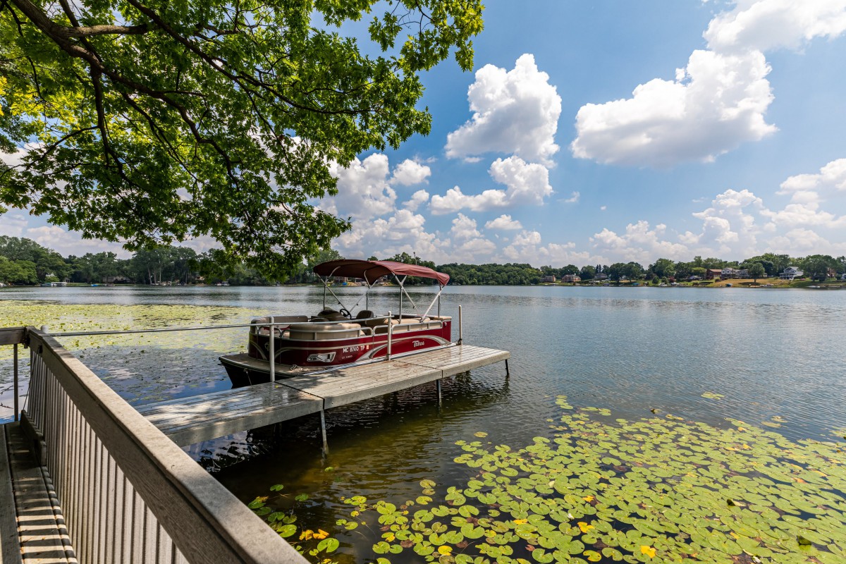 A serene lake scene with a docked boat and water lilies under a clear, blue sky.