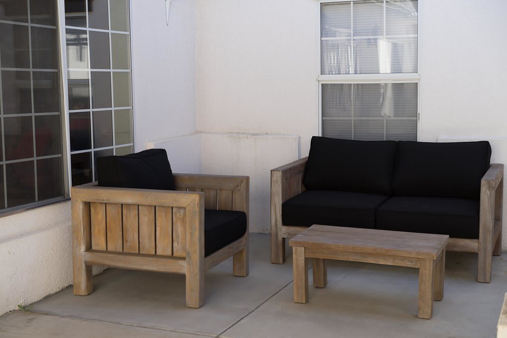 A patio set with wooden chairs, a sofa, and a coffee table featuring black cushions.