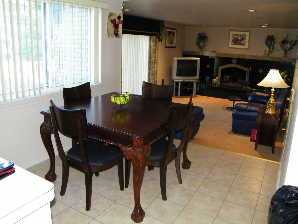 A dining area with a wooden table and chairs, adjacent to a living room featuring a television and fireplace.
