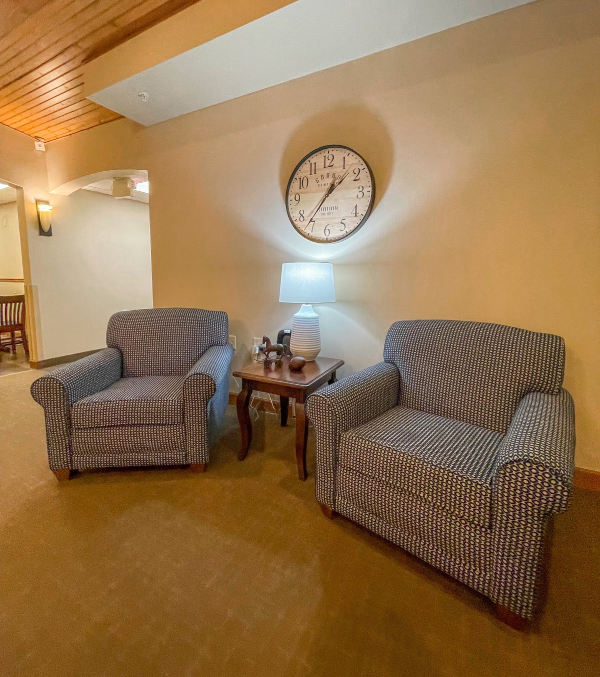 A cozy living room setting with two upholstered chairs, a small side table, and a large wall clock.