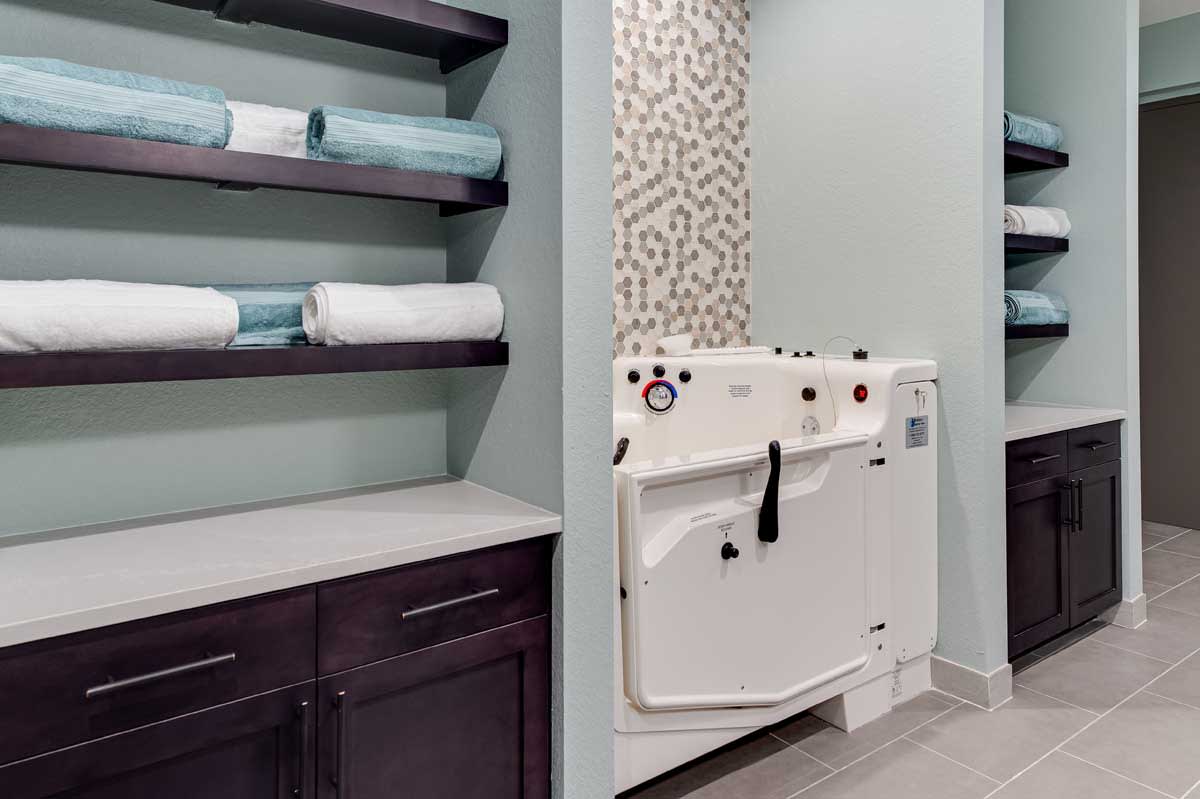 A modern bathroom featuring a specialized bathtub and neatly arranged shelves with towels.