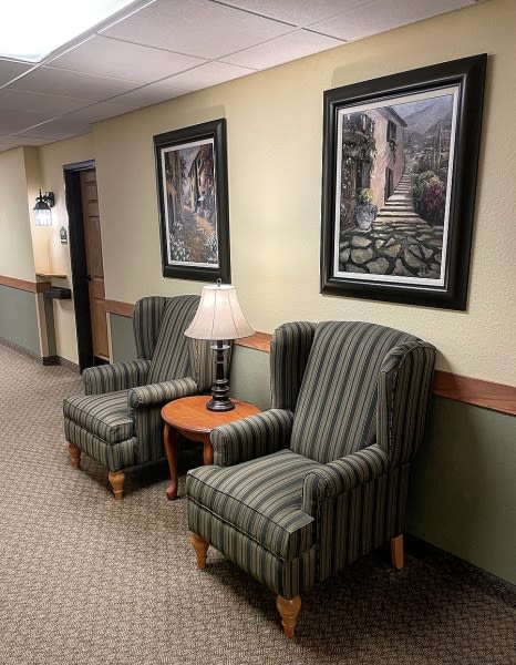 A cozy hallway seating area with two striped chairs, a small wooden table, and framed artwork on the wall.
