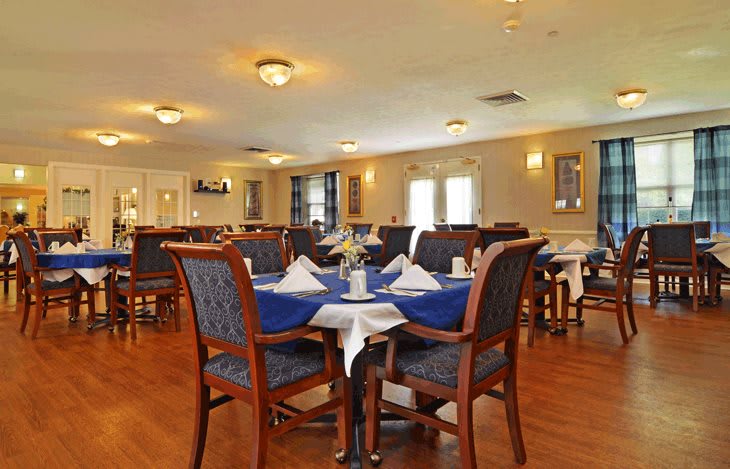 A spacious dining room with neatly arranged tables and chairs, featuring blue tablecloths and elegant decor.