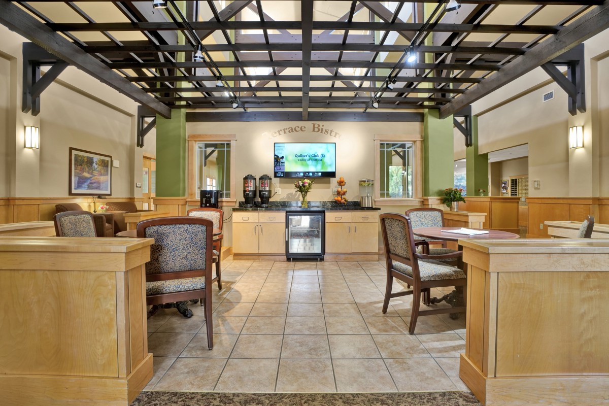 A modern lobby seating area with a television, tables, and chairs under a unique ceiling structure.