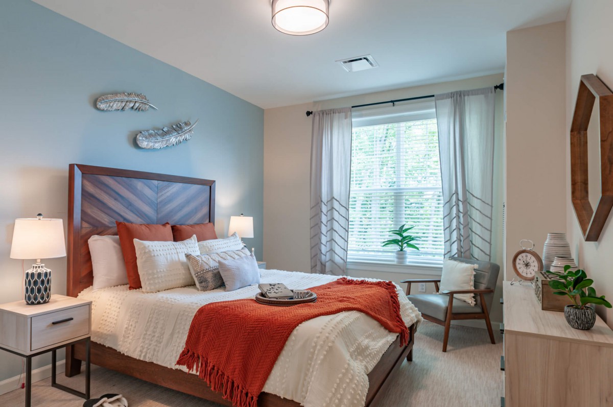 A modern and cozy bedroom with orange accents and ample natural light.